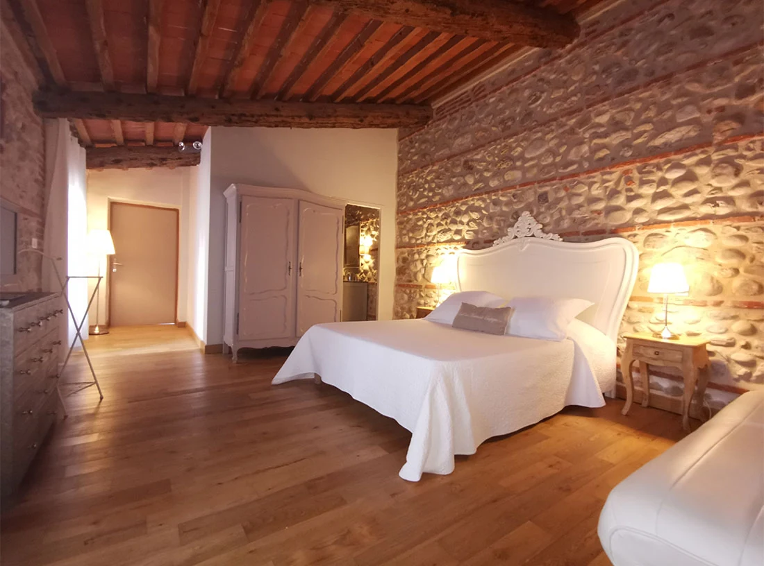 Une chambre du gîte avec lit double, murs en pierre et plafond en bois